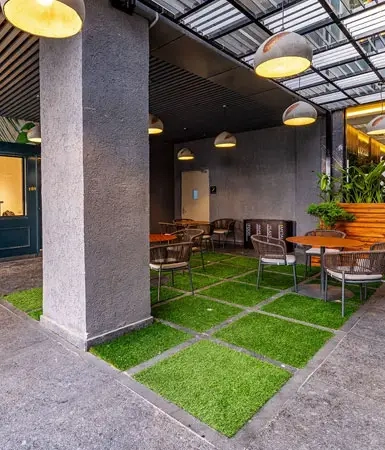 Outdoor seating area at the restaurant, with green grass flooring and modern lighting, located at Good Earth Business Bay I, Gurugram, a mixed-use commercial building.