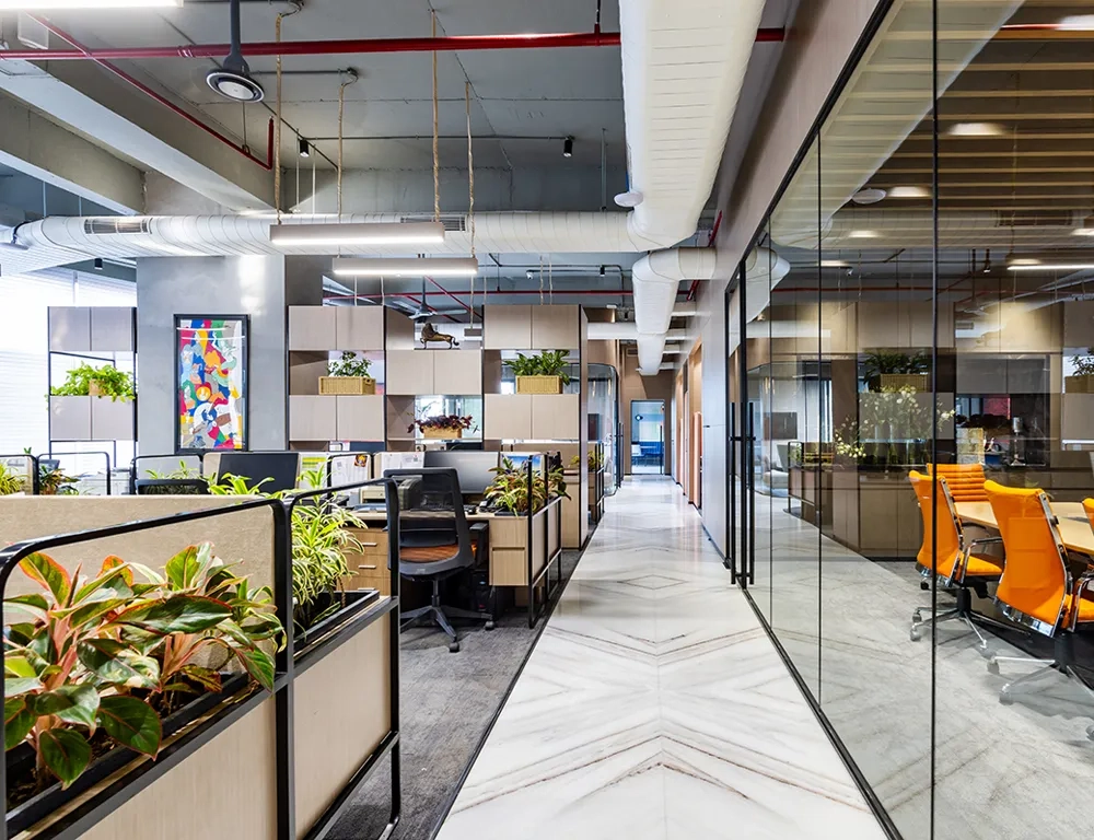 Corridor view at Good Earth Infra with glass-partitioned meeting rooms and well-organised workstations, showcasing an office layout.